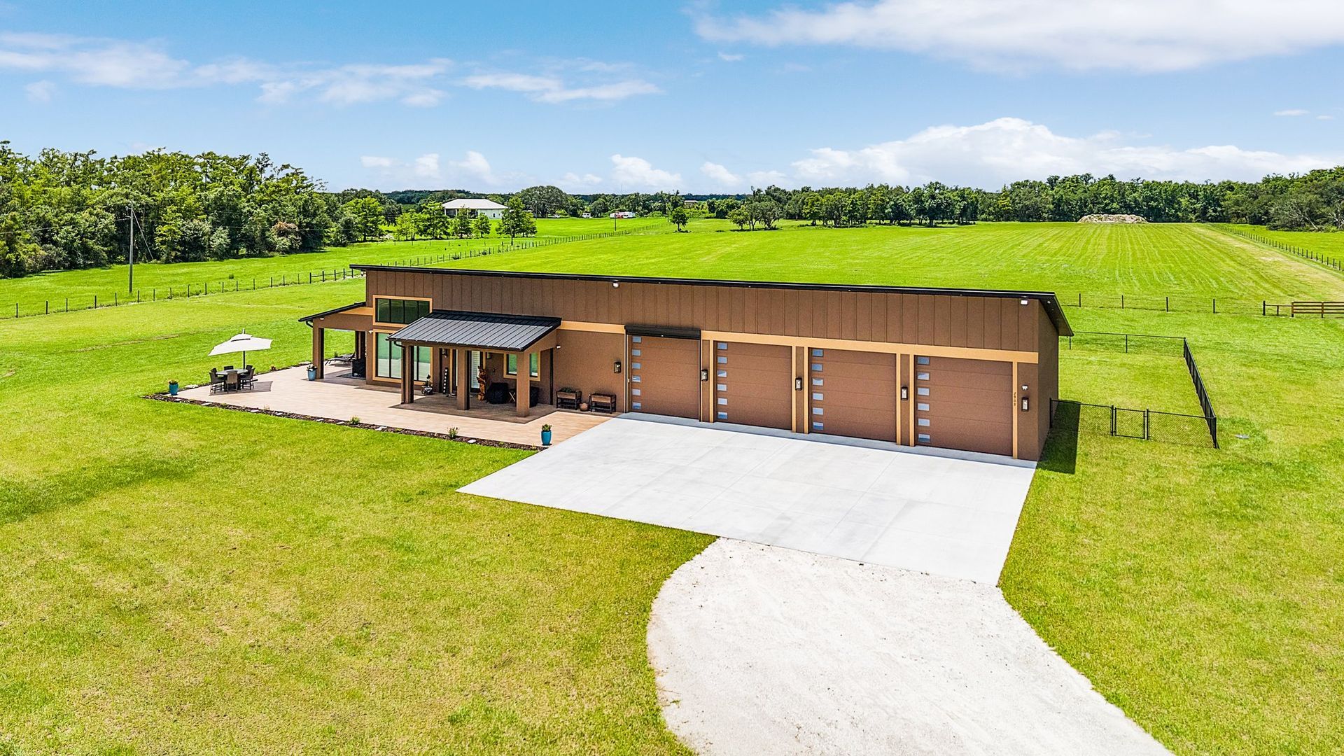 Brown building with multiple garage doors on a grassy field with a long driveway.