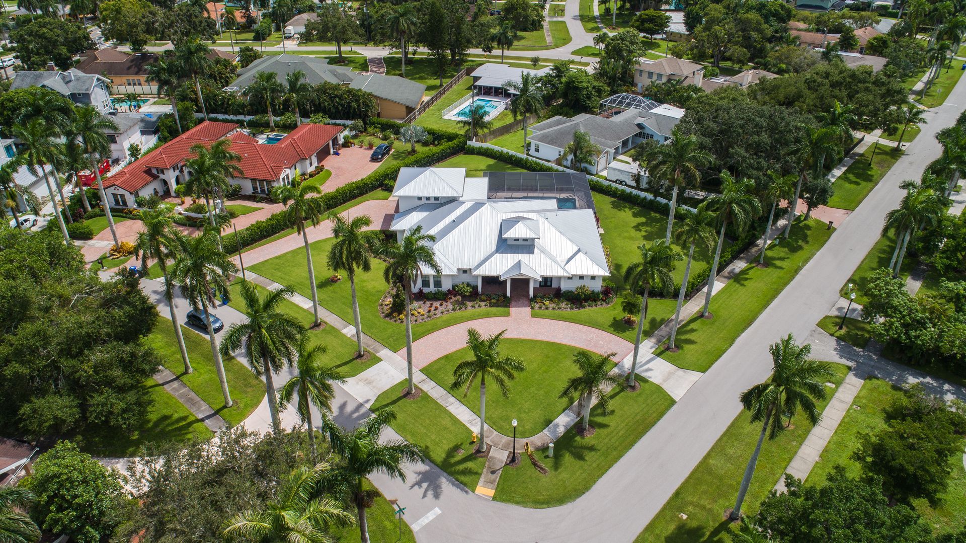 Aerial view of luxury houses with palm trees lining driveways and green lawns.