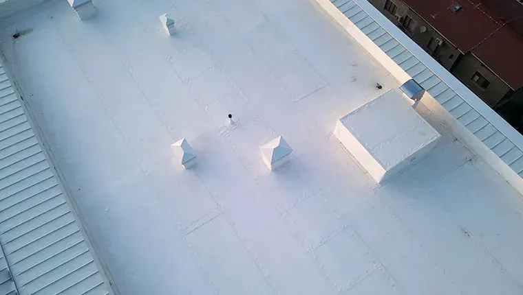 White commercial roof with vents and a small building.