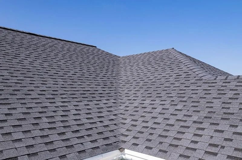 Gray asphalt shingle roof against a clear blue sky.
