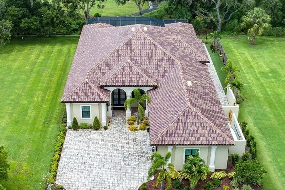 Overhead view of a beige and brown home with a brick driveway, surrounded by green grass and trees.