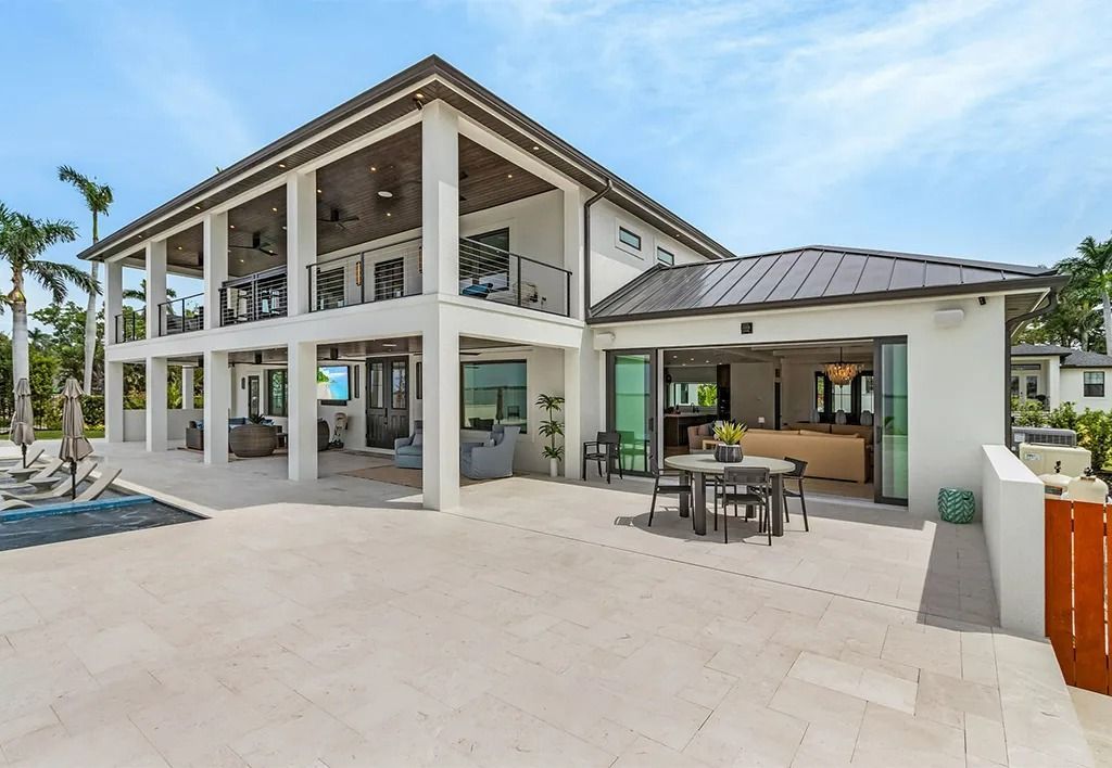 Two-story white house with large patio, black railings, and a dark roof under a blue sky.