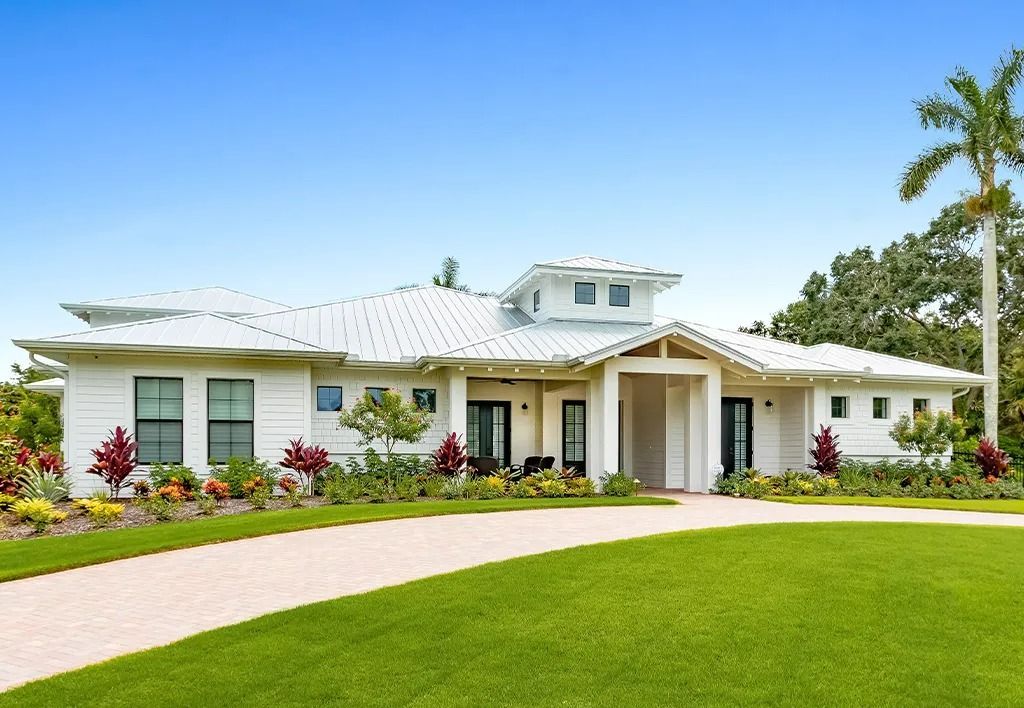 White house with a green lawn and circular driveway under a clear blue sky.