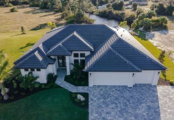 Modern white house with dark gray tile roof, paver driveway, and landscaping.