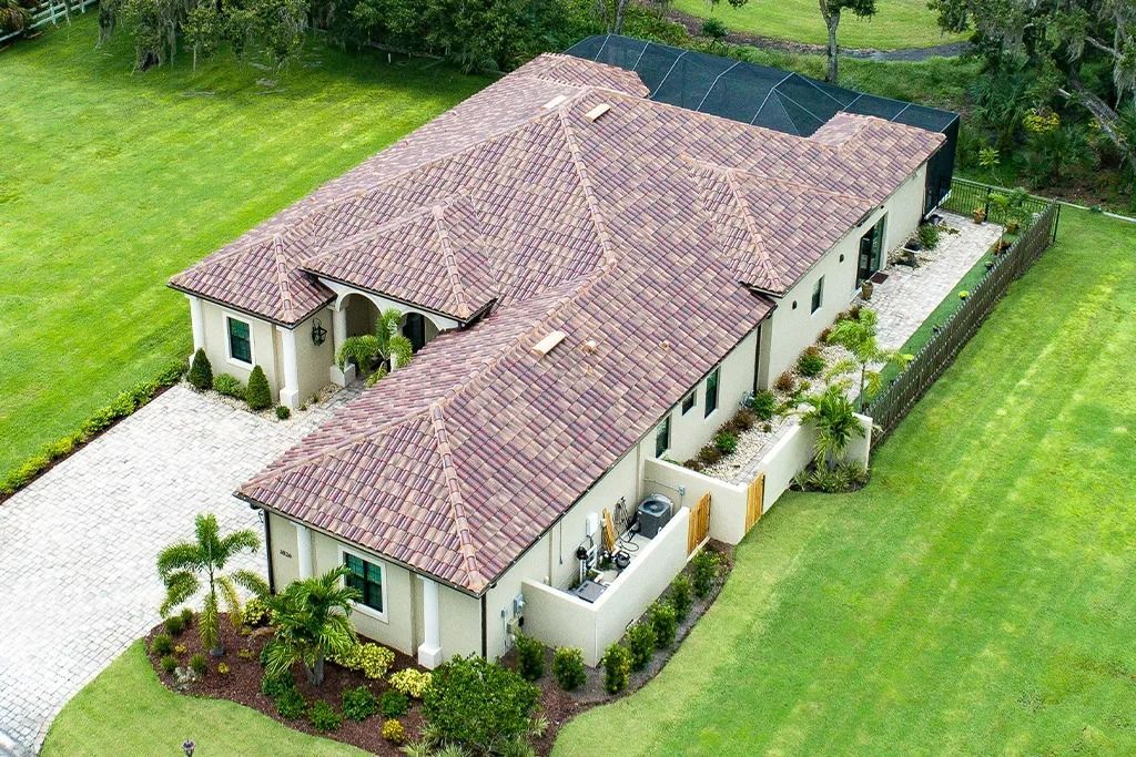 Beige house with a terracotta roof, a white driveway, and green lawn.