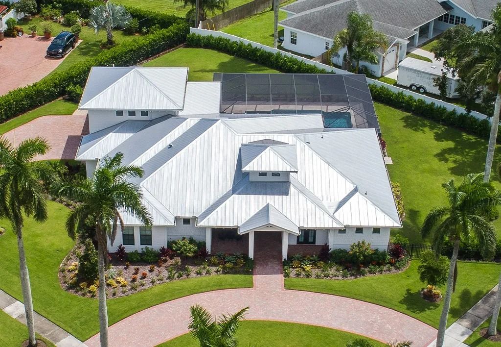 Aerial view of a white modern house with a pool, red brick driveway, and green lawn.