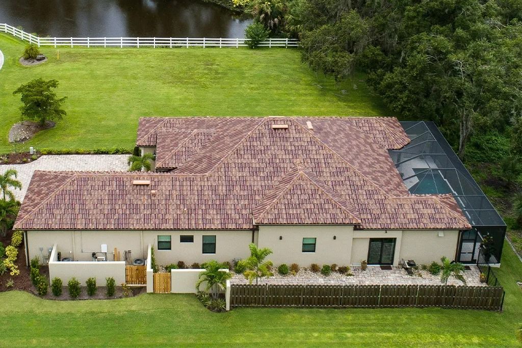 Aerial view of a single-story house with a clay tile roof and a pool enclosure, surrounded by green grass.