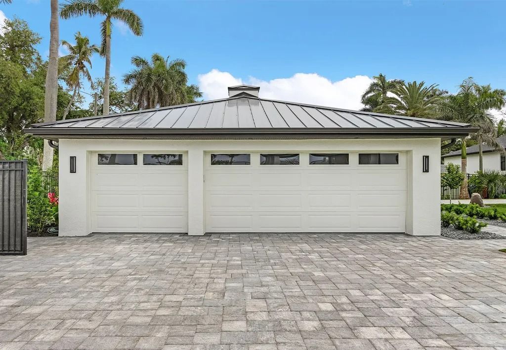 Two-car garage with white doors, black roof, and brick driveway under a blue sky.