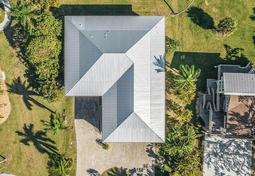 Overhead view of a modern house with a gray metal roof, surrounded by green grass and landscaping.