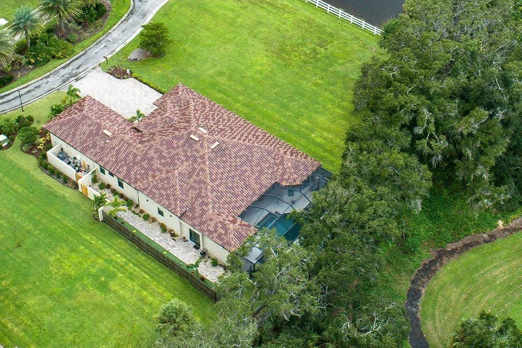 Aerial view of a large house with a tile roof surrounded by green grass and trees.