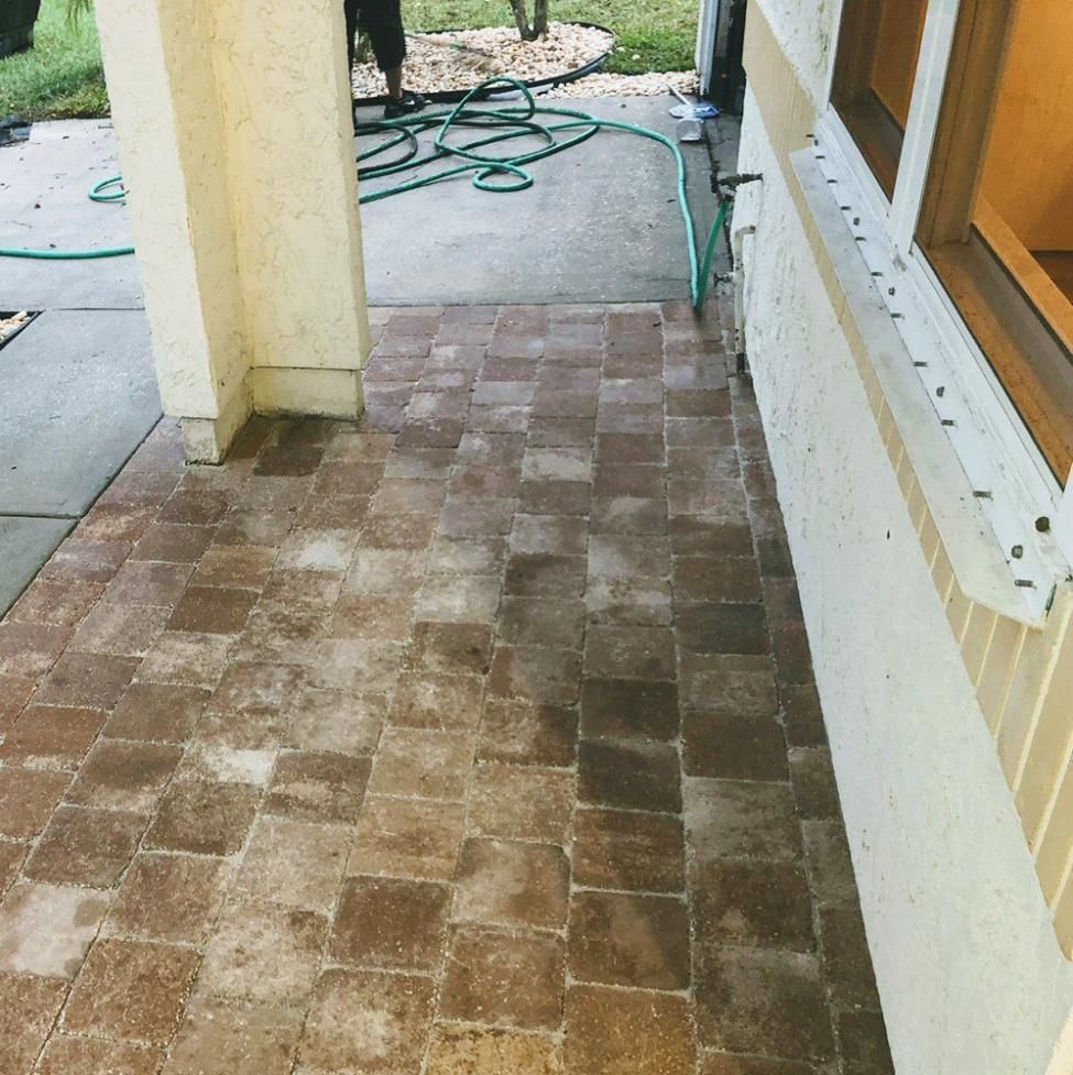 Brick-paved patio walkway beside a house with a garden hose and columns