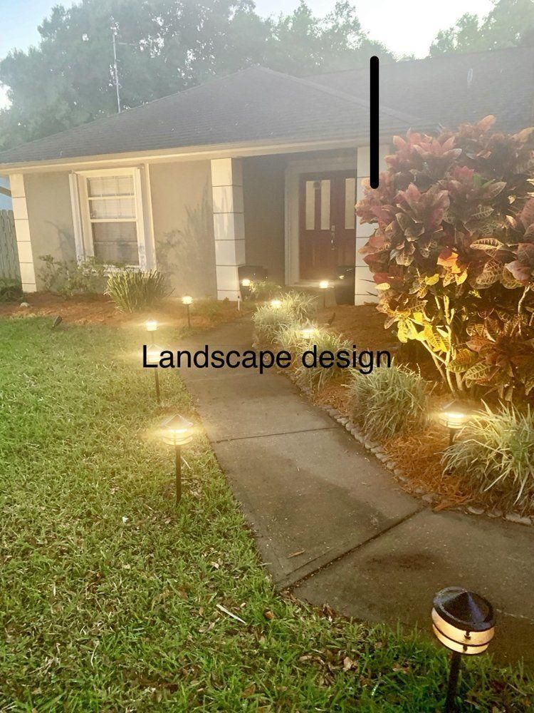 Front yard at dusk with lit walkway, landscaped plants, and a small house porch.