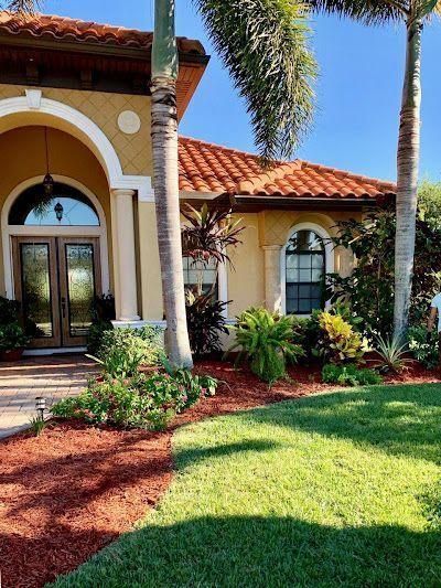 Sunlit Mediterranean-style house entrance with arched doorway, palm trees, and manicured lawn