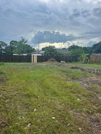 Grassy vacant lot with muddy ground, a fence, and dark storm clouds overhead