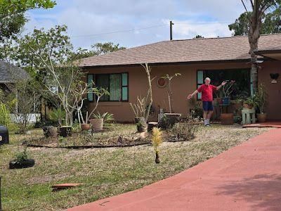 Person standing in front of a brown house with a red driveway and desert landscaping