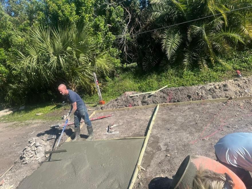 Worker smoothing wet concrete outdoors beside greenery
