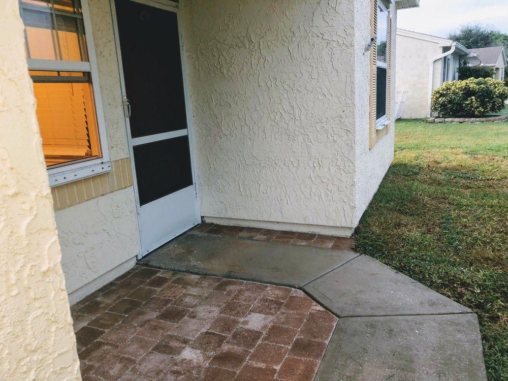 Patio entrance with brick and concrete walkway beside a stucco house and screened door