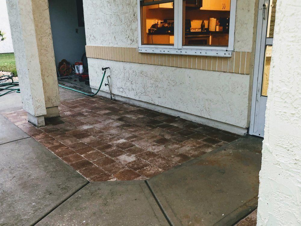 Small wet patio with tiled section, concrete walkway, white stucco columns, and a lit window.