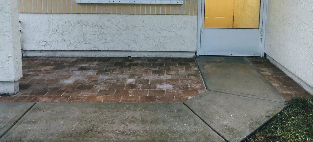 Front entry patio with cracked concrete, brick pavers, and a yellow-lit door at dusk