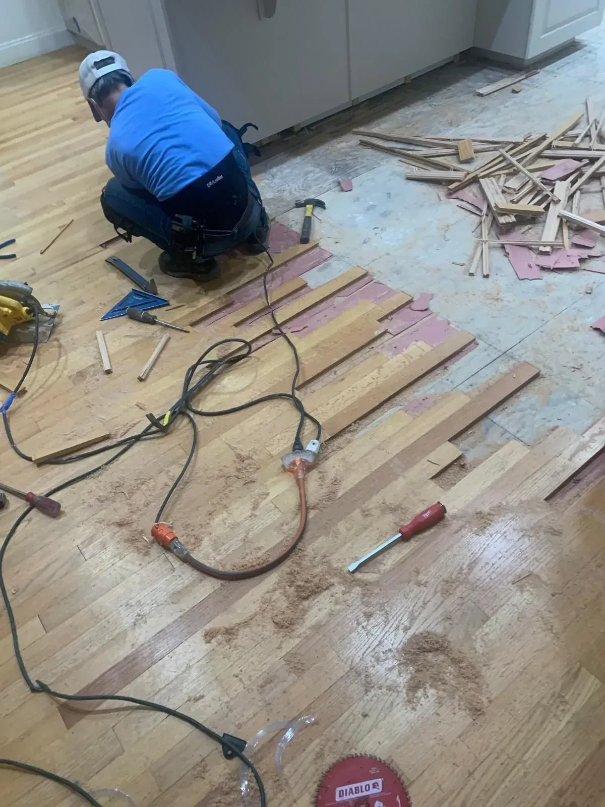 Man removing wood floor with tools in a kitchen.