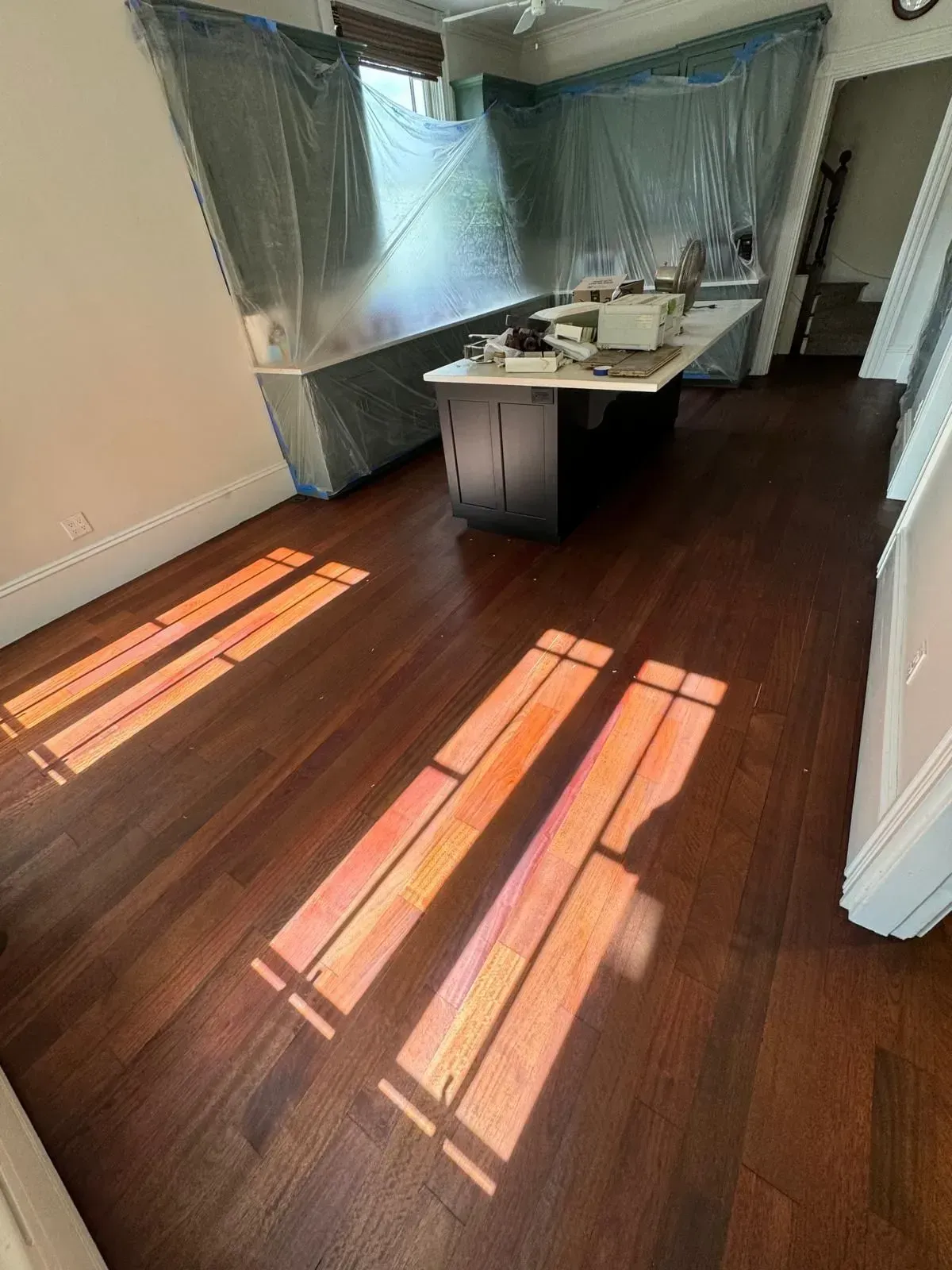 Sunlight streams across dark wood flooring in a room with covered countertops and a dark island.