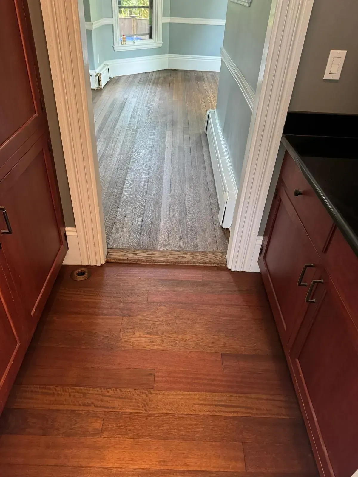 Wooden floors in a doorway framed by cabinets with red doors, leading to another room.