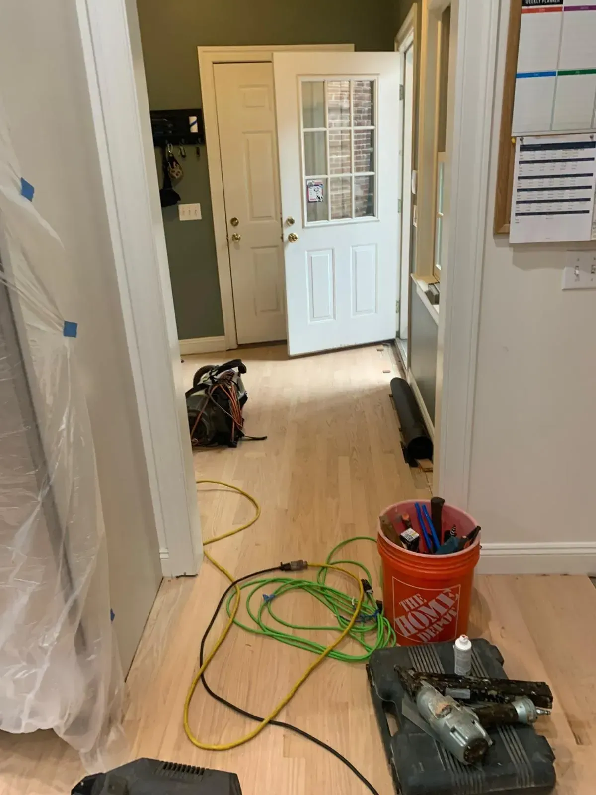 Hallway with newly installed light wood flooring, tools, door open to outside.