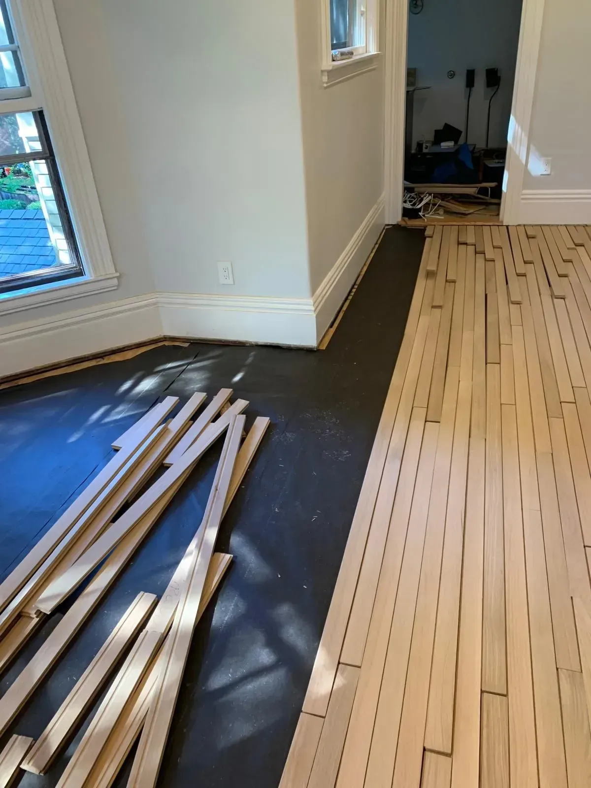 Wooden floor being installed. Boards are laid down beside a room with blue walls.