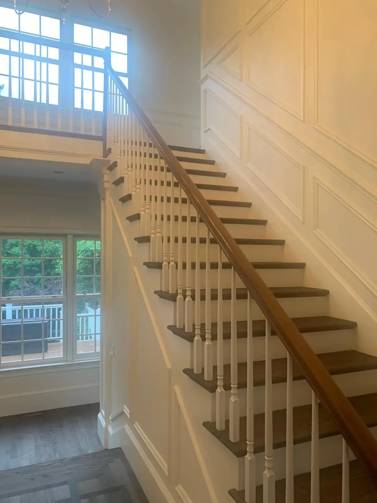 Staircase with white banister, wooden steps, and paneling. Bright sunlight streams in from a window.