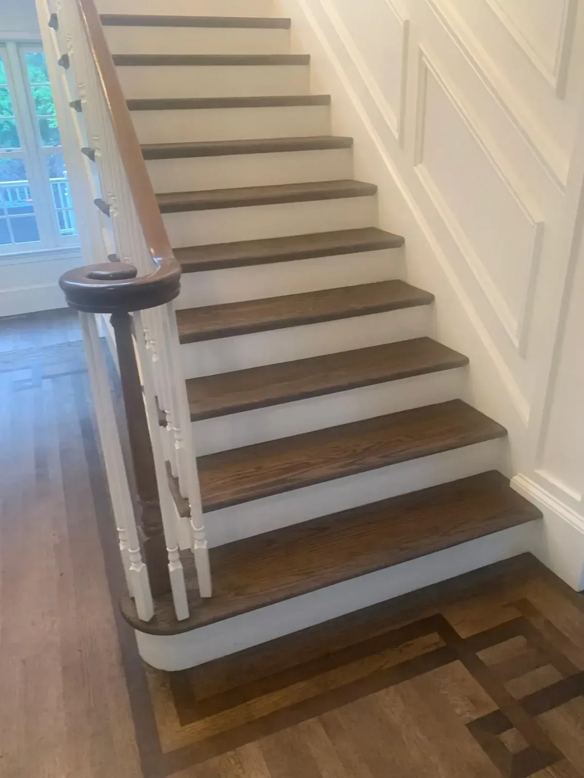 Wooden staircase with white risers, dark treads, and wood handrail. Entryway with decorative flooring.
