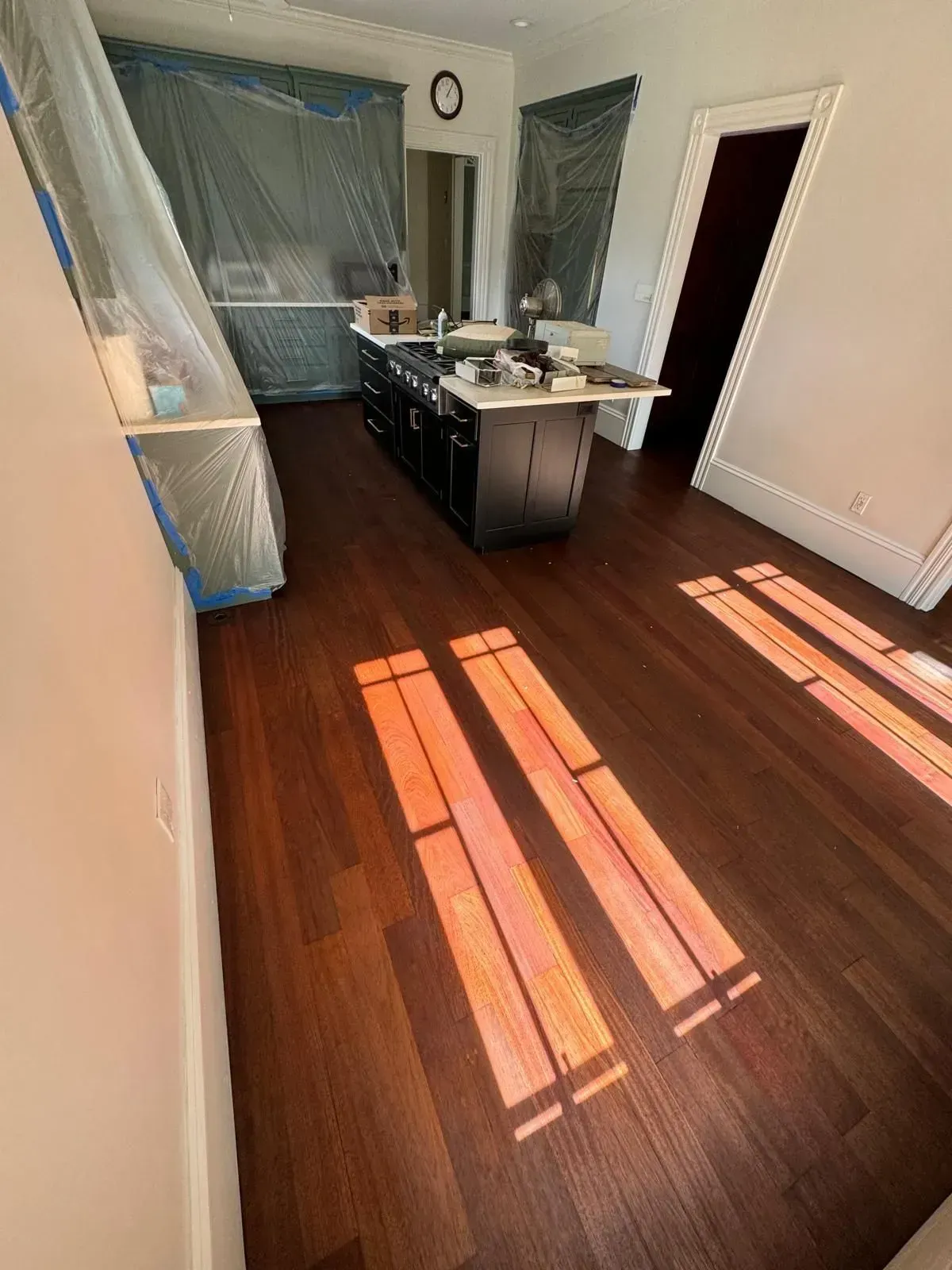 Kitchen with dark wood floors, black island, and sunlight streaming through the windows, covered in plastic.