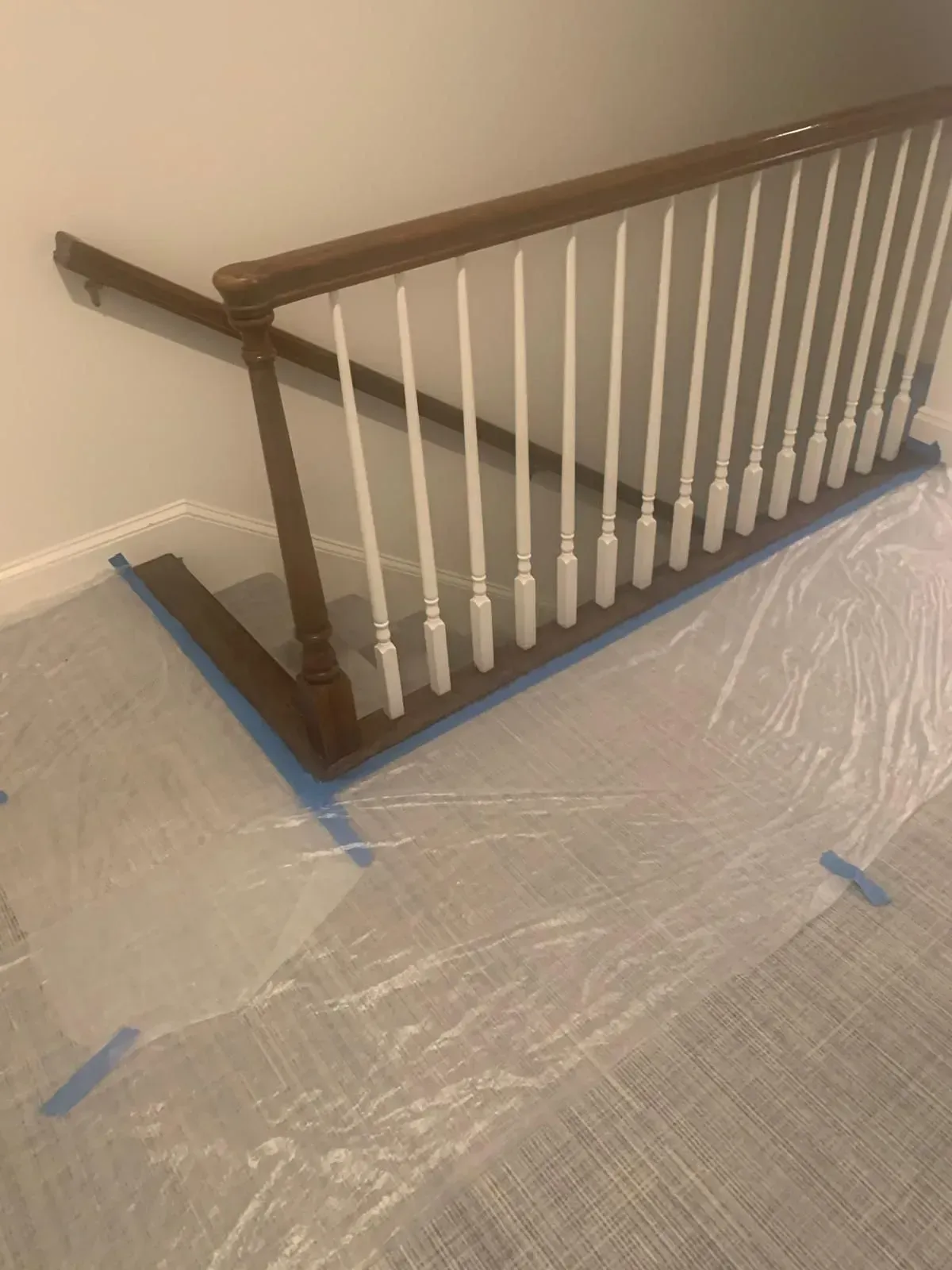 Wooden stair railing with white spindles, covered flooring for painting.