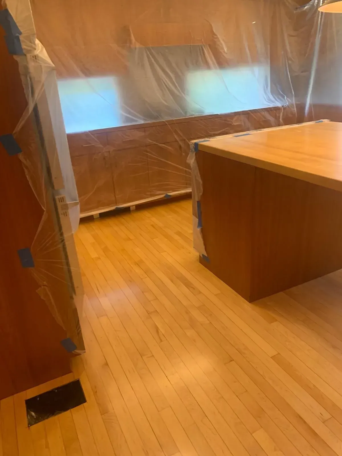 Kitchen with hardwood floors, cabinetry, and an island. Surfaces are covered in plastic for protection.