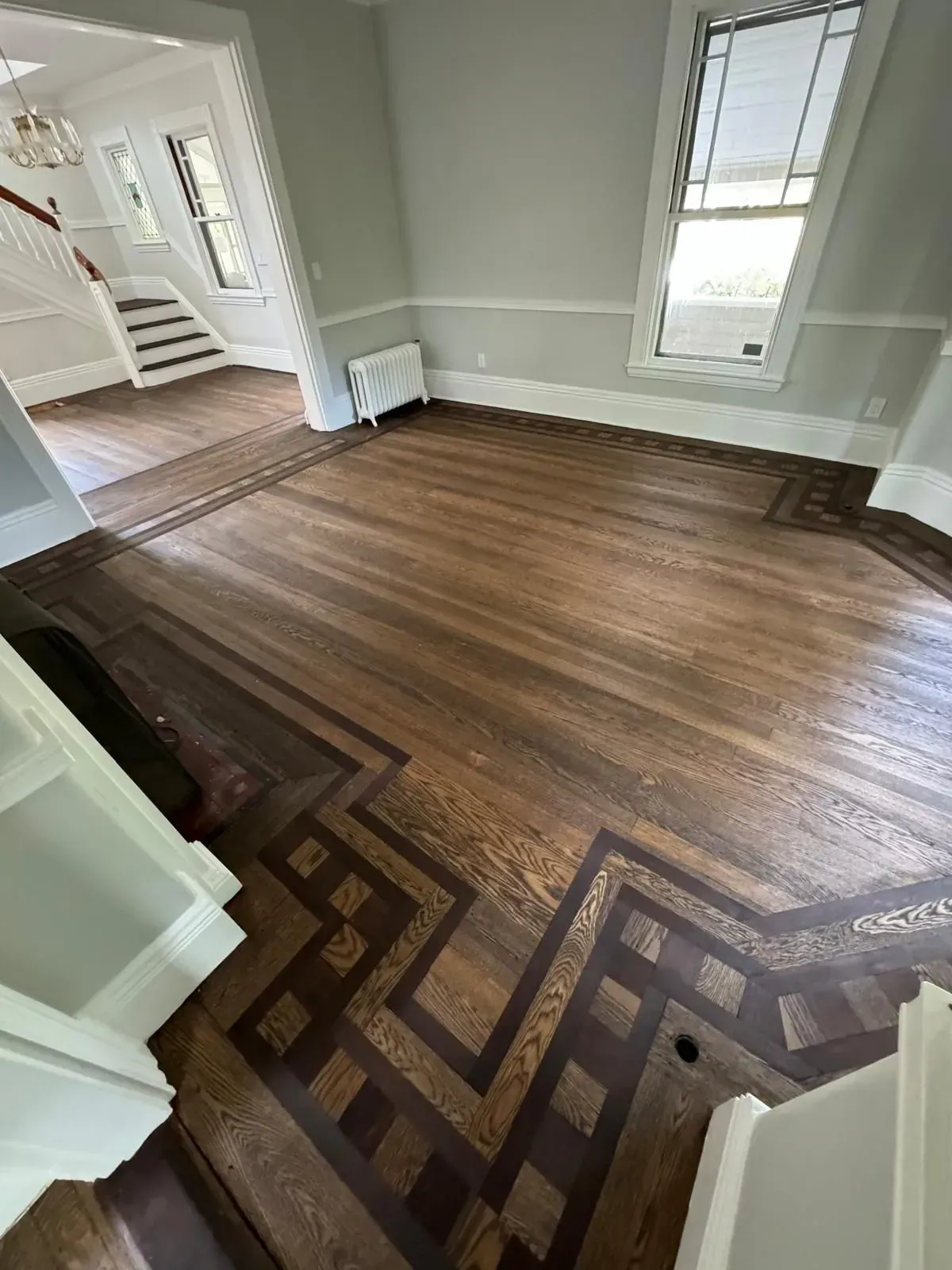 Wooden floor with intricate dark and light geometric patterns in a room with a staircase and window.