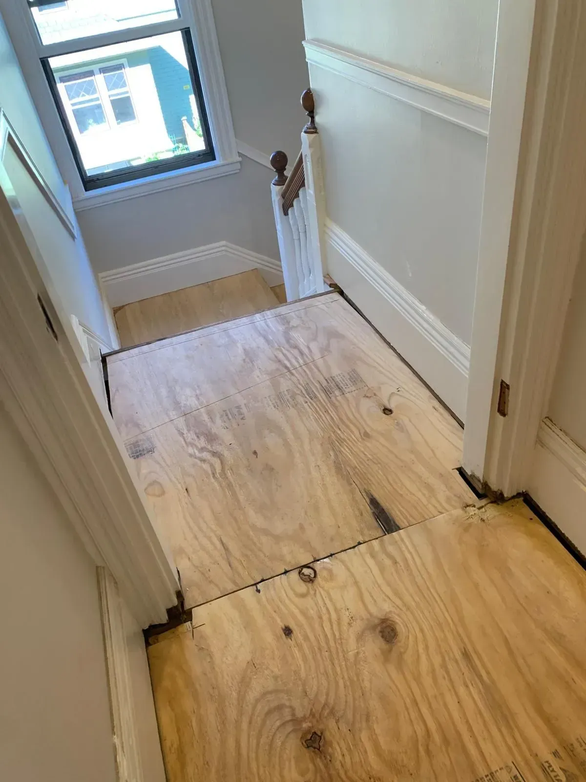 Wooden stairs leading down with a plywood floor landing and white trim.