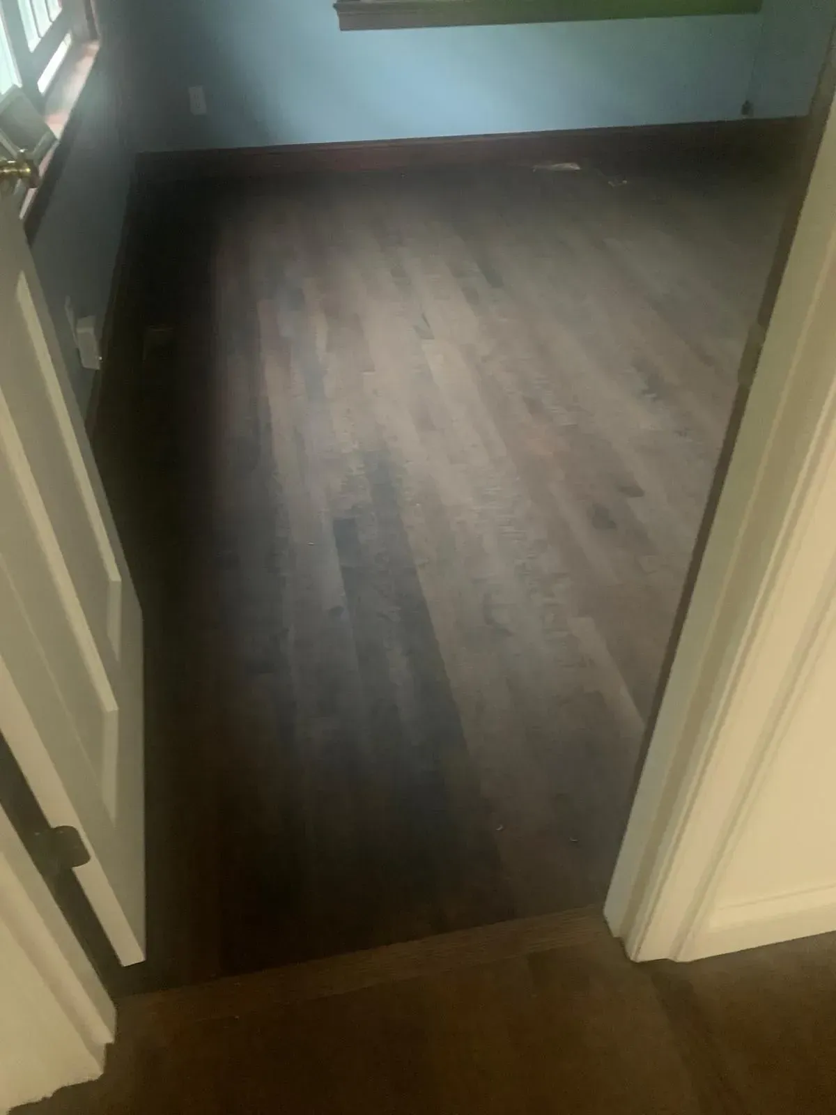 Dark wood floor in a room, viewed from doorway. Light from unseen window brightens the space.