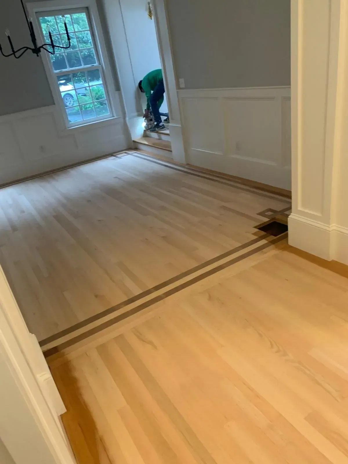 Newly installed hardwood flooring with a border. A person is working in the doorway.
