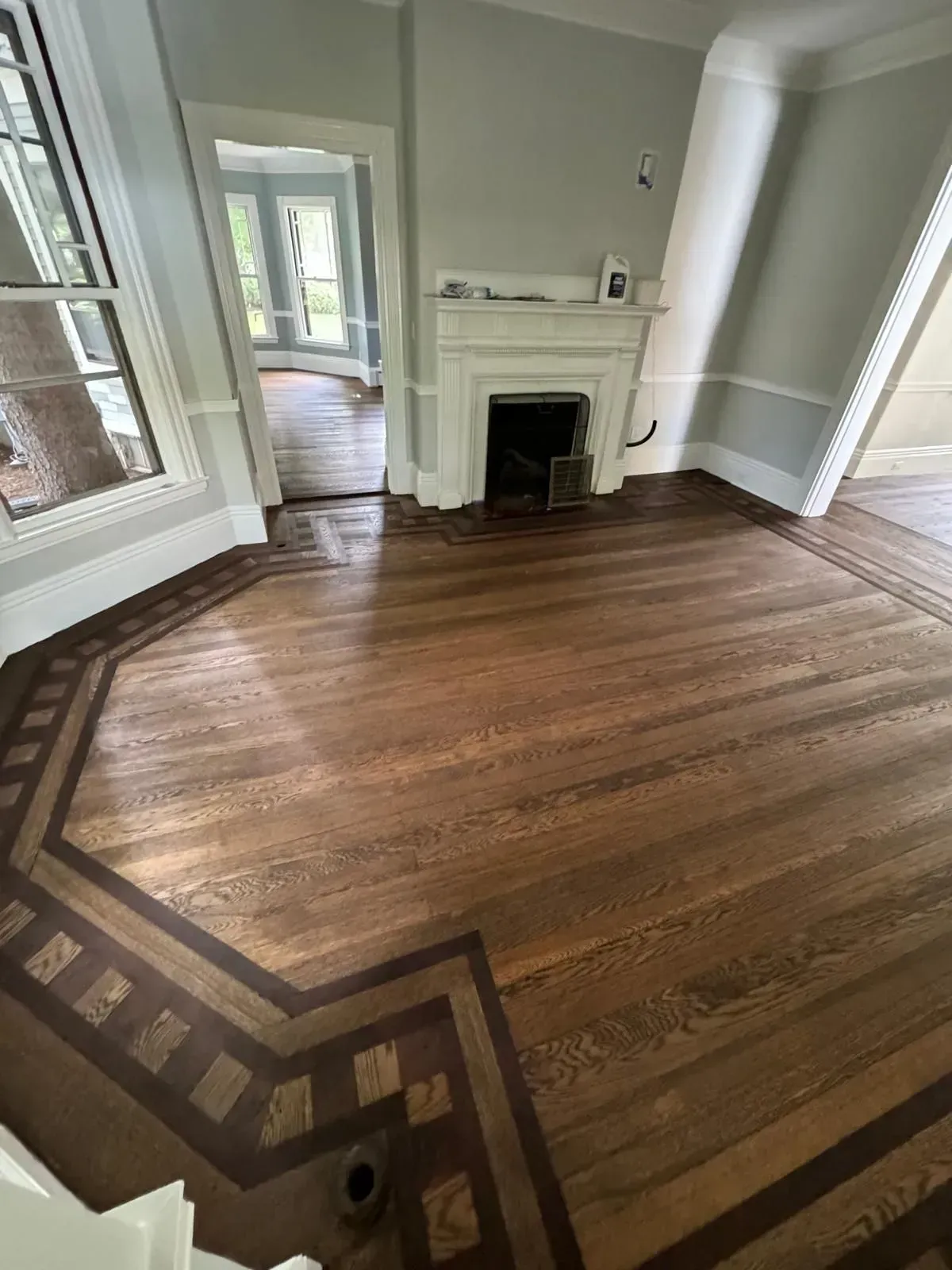 Hardwood floor with dark border, light walls, and fireplace. Room with doorway to another room.