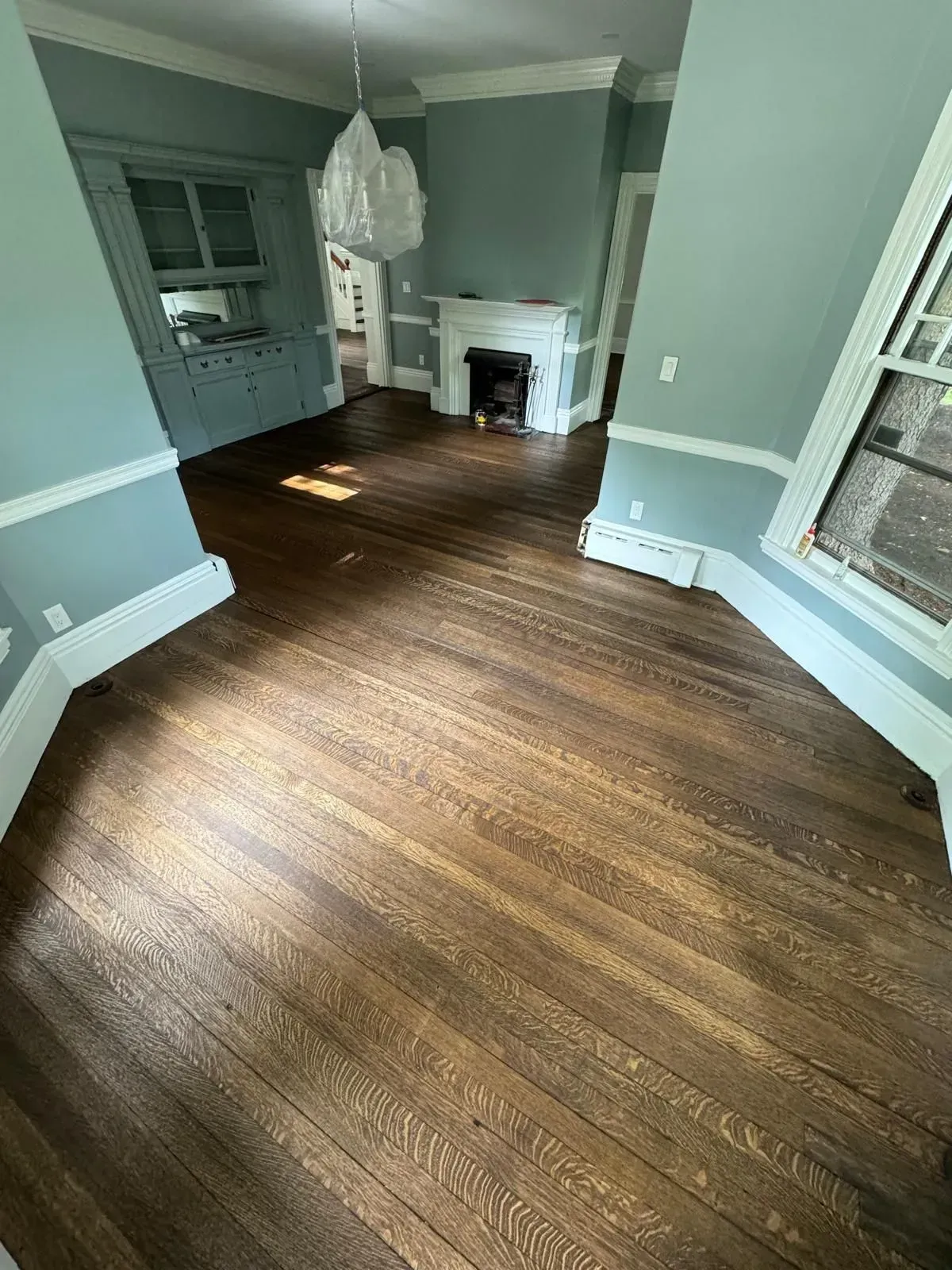 Wood floors in a room with blue walls, white trim, a fireplace, and a built-in cabinet.