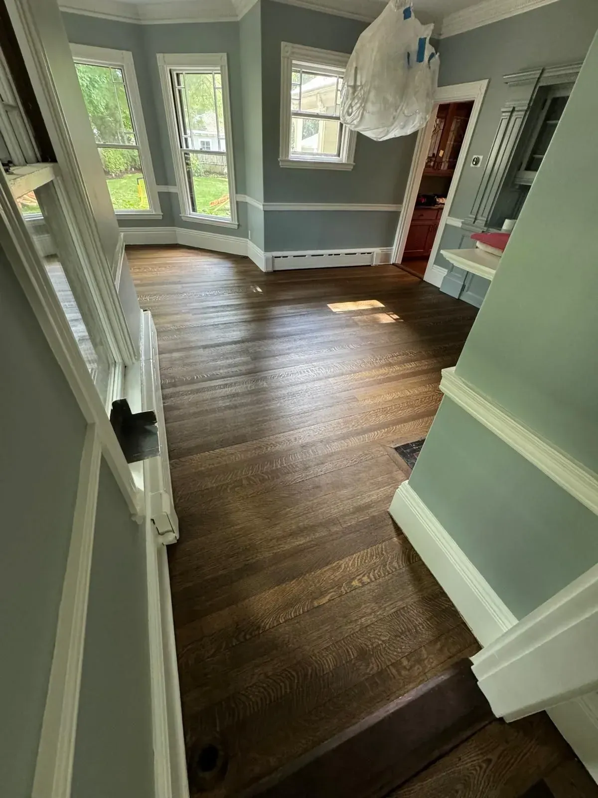 Hardwood floor with light streaming through windows. Pale blue walls, white trim, and a dark wood door.