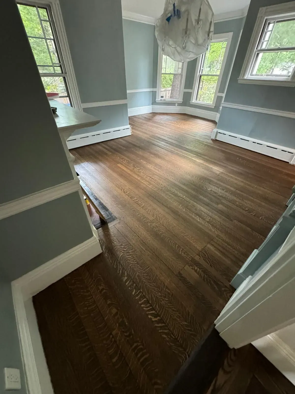 Dark stained hardwood floor in a room with blue-gray walls and white trim.