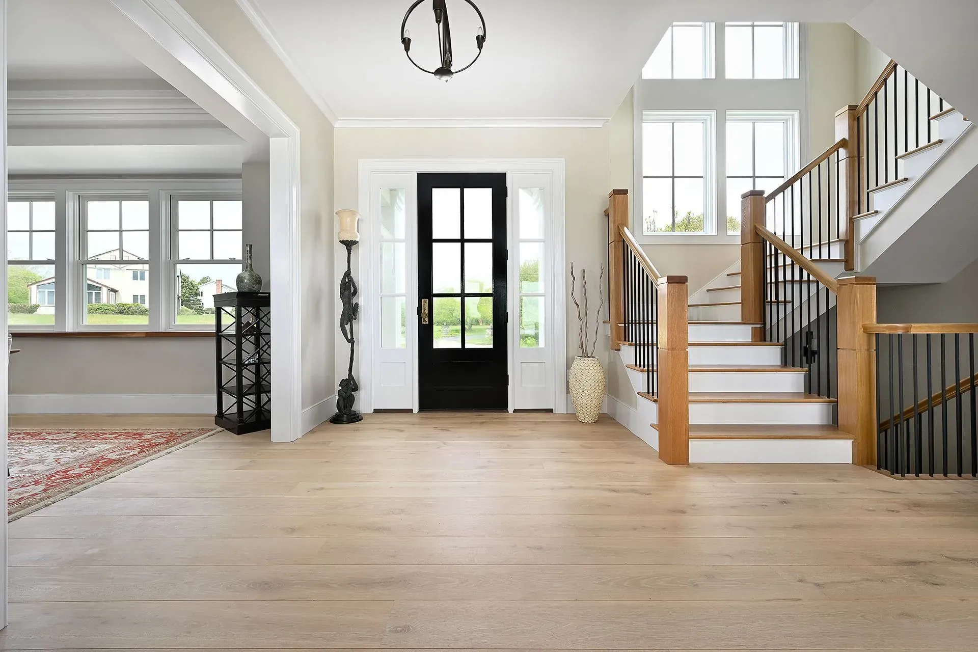 Bright entryway with hardwood floors, staircase, black front door, and windows.