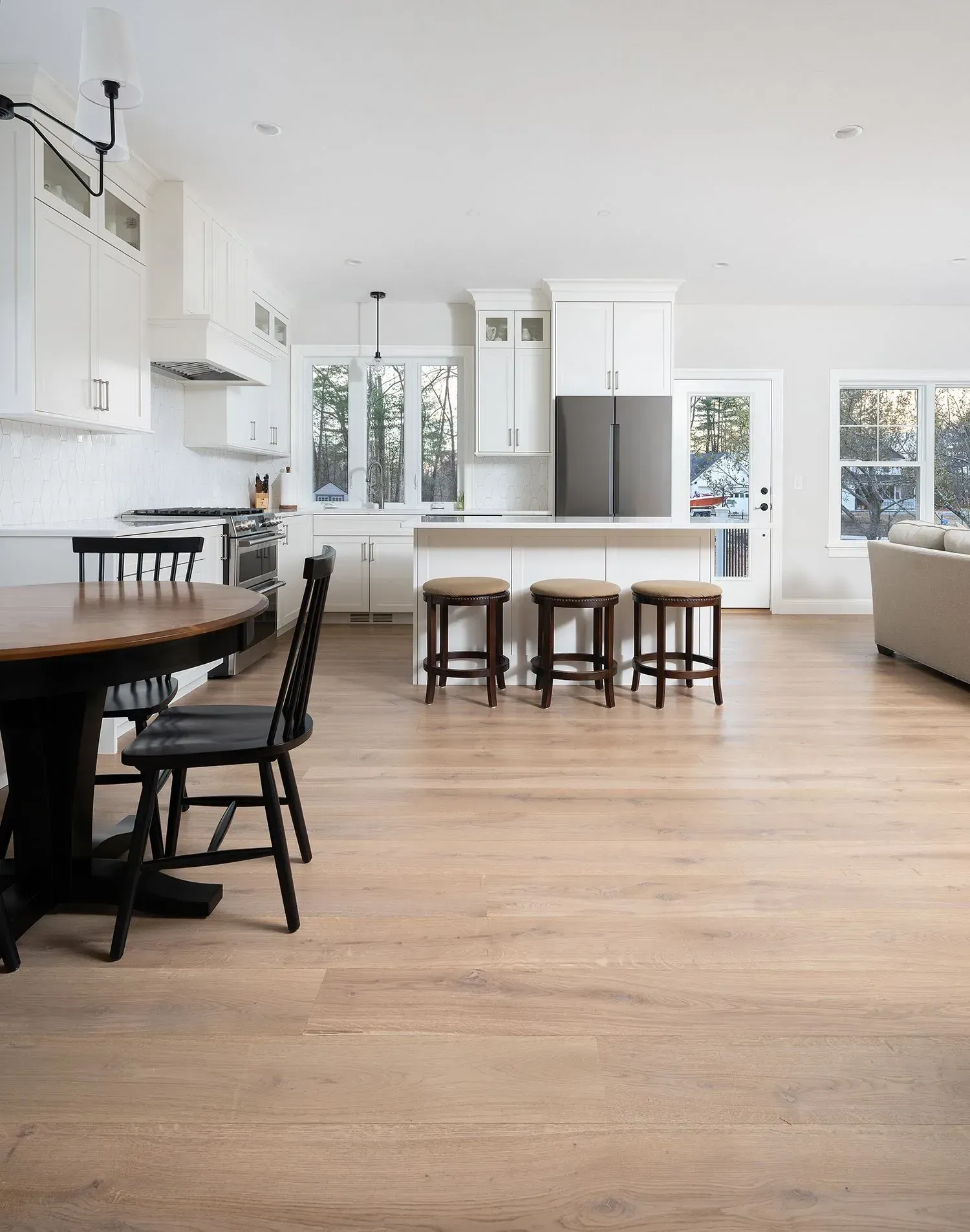 Bright kitchen with white cabinets, island with stools, and a dark dining table; light wood floors.