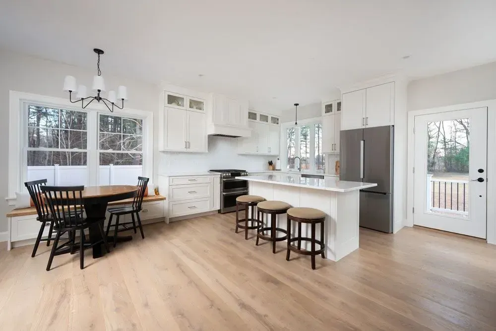 Bright, white kitchen with island, table, and stainless steel appliances. Light wood floor.