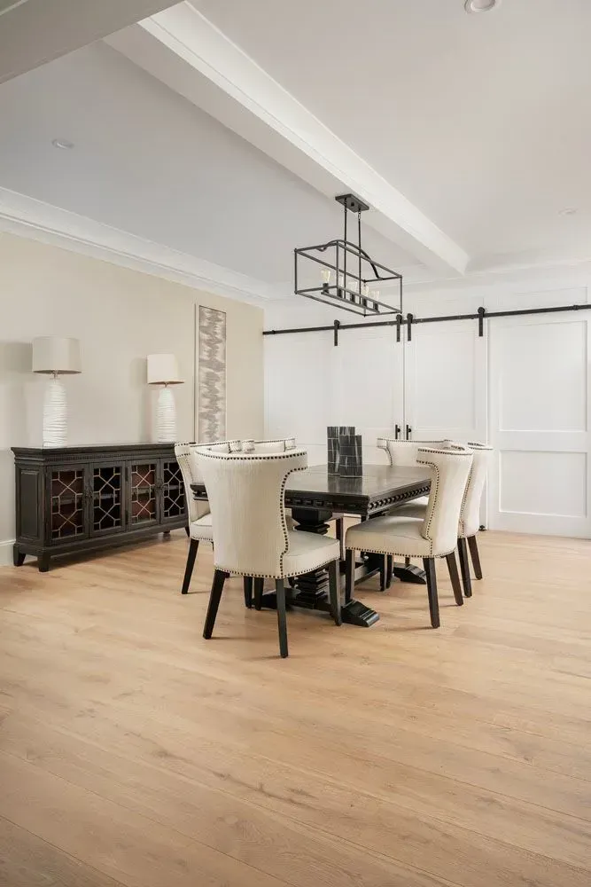 Formal dining room with a table, chairs, sideboard, and barn doors. Light wood floor.