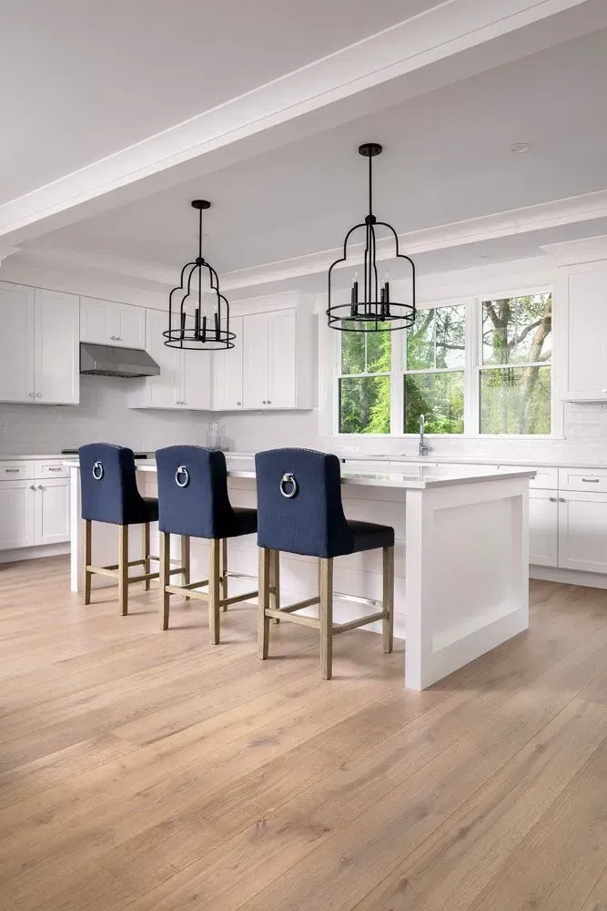 Modern white kitchen with island, blue bar stools, and decorative light fixtures. Light wood floors.