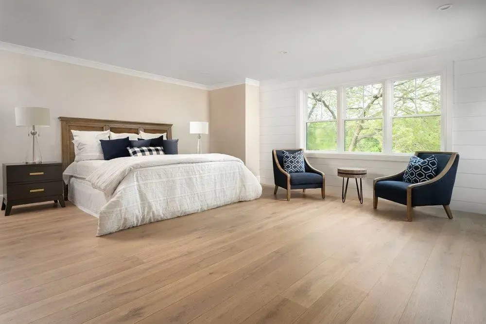 Spacious bedroom with a wooden bed, two armchairs, and a large window overlooking greenery.