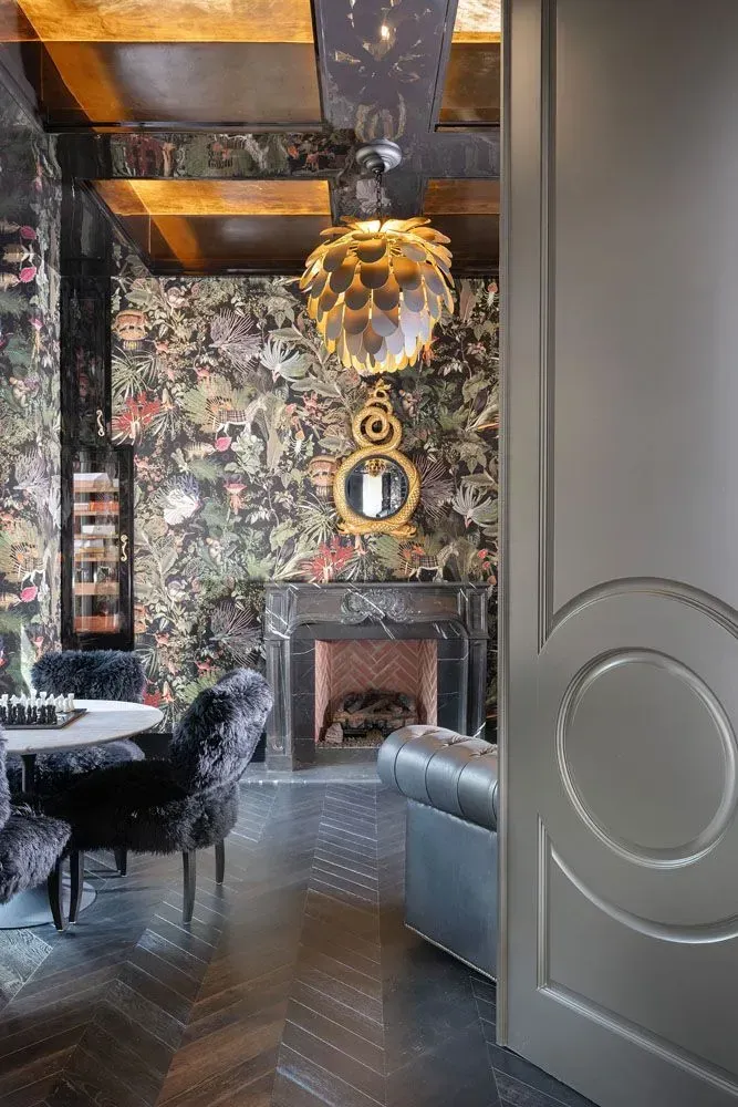 Luxurious dining room with patterned wallpaper, black velvet chairs, fireplace, and ornate gold chandelier.
