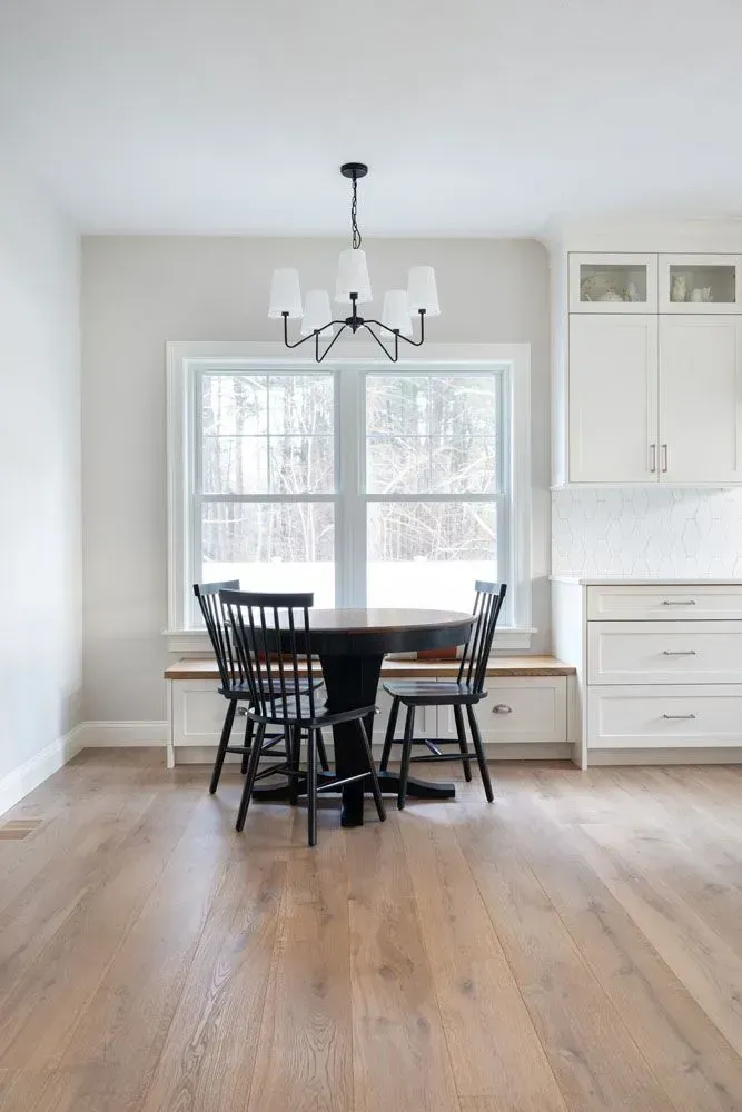 Dining area with round black table, black chairs, and white cabinets near a window.