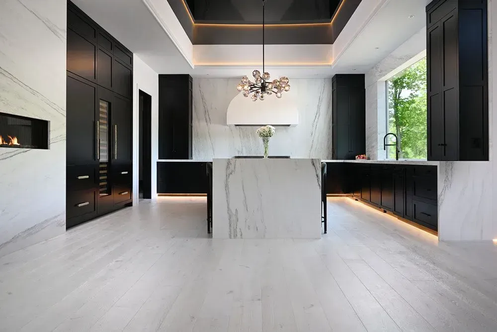 Modern kitchen with marble island and counters, black cabinets, and white flooring.
